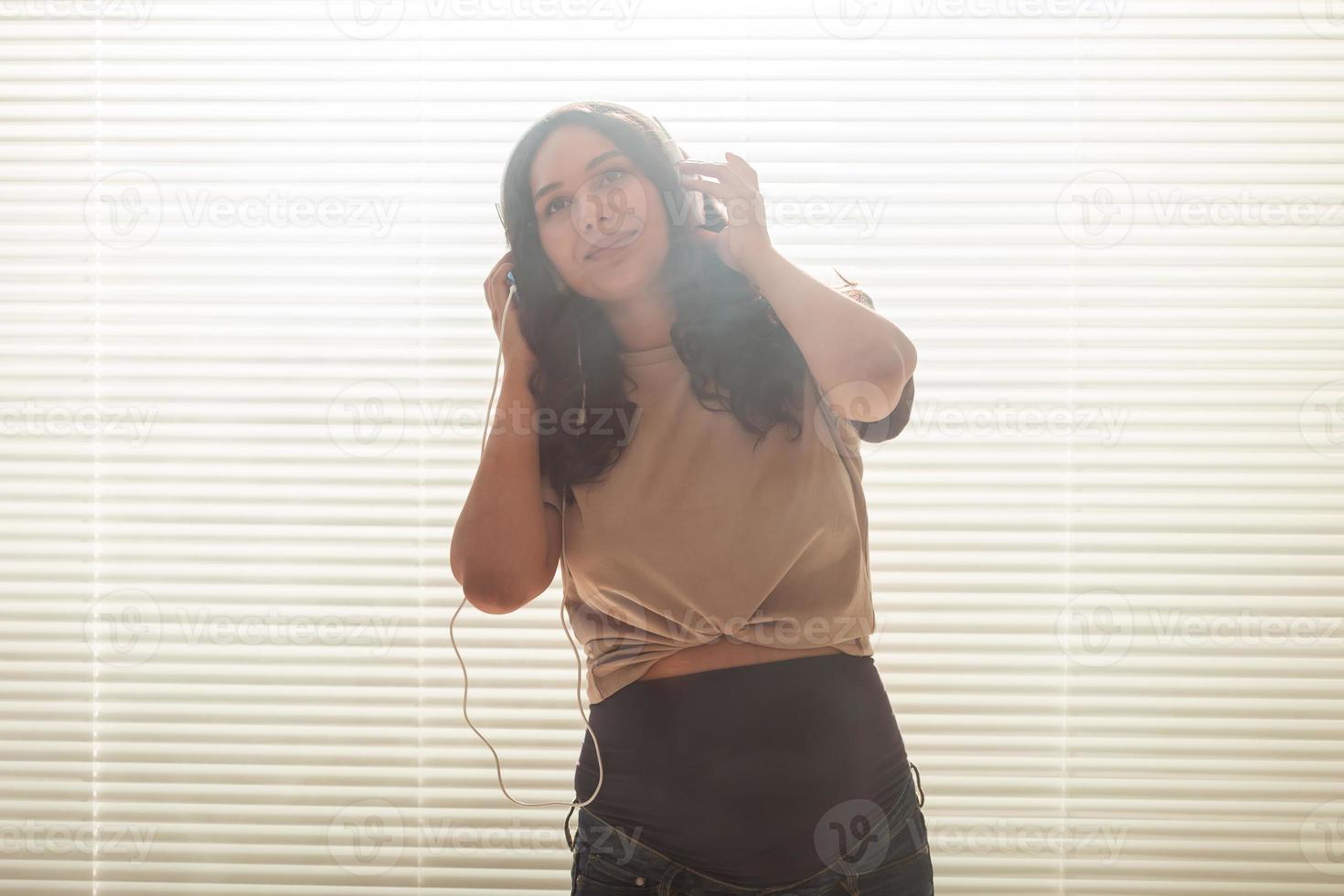 Portrait of pregnant woman near window at home and listening music in headphones. Pregnancy and leisure concept. photo