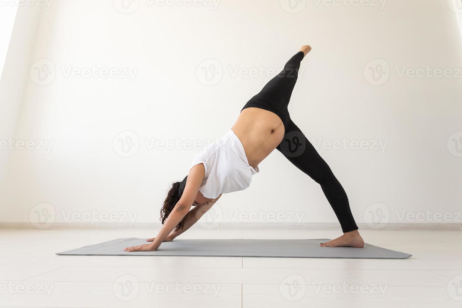 Young flexible pregnant woman doing gymnastics on rug on the floor on white background. The concept of preparing the body for easy childbirth. Copy space. photo