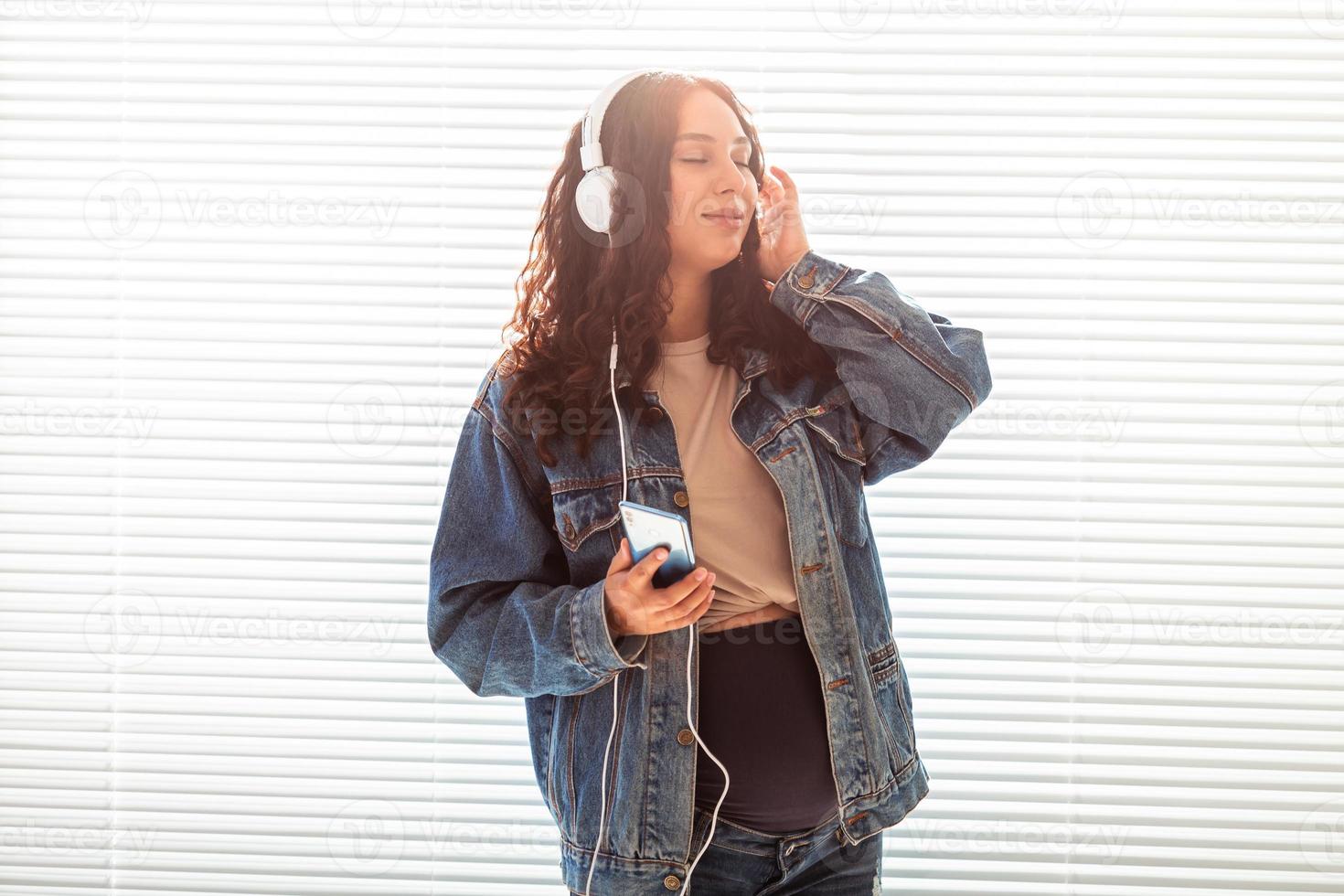 Beautiful young peaceful pregnant woman listens to pleasant classical music using smartphone and headphones. Concept of positive attitude before childbirth photo