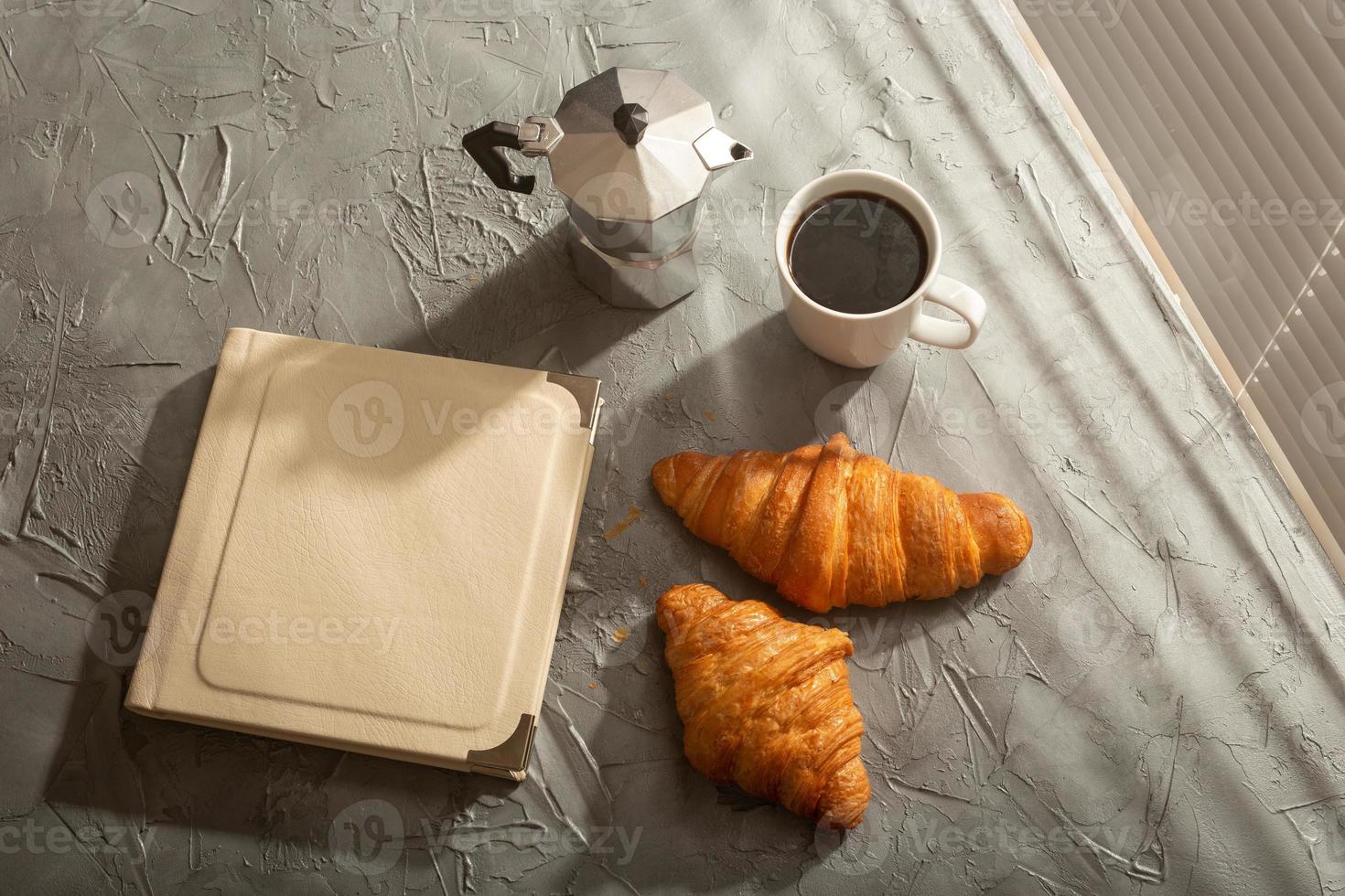 naturaleza muerta para una agradable taza de café por la mañana y croissants con un libro sobre la mesa. concepto de descanso para almorzar o comenzar la mañana foto