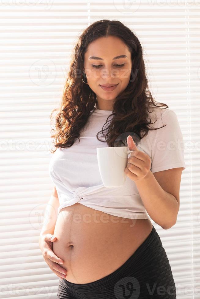 feliz embarazada joven bella mujer bebe té durante el desayuno de la mañana. licencia por embarazo y maternidad. foto