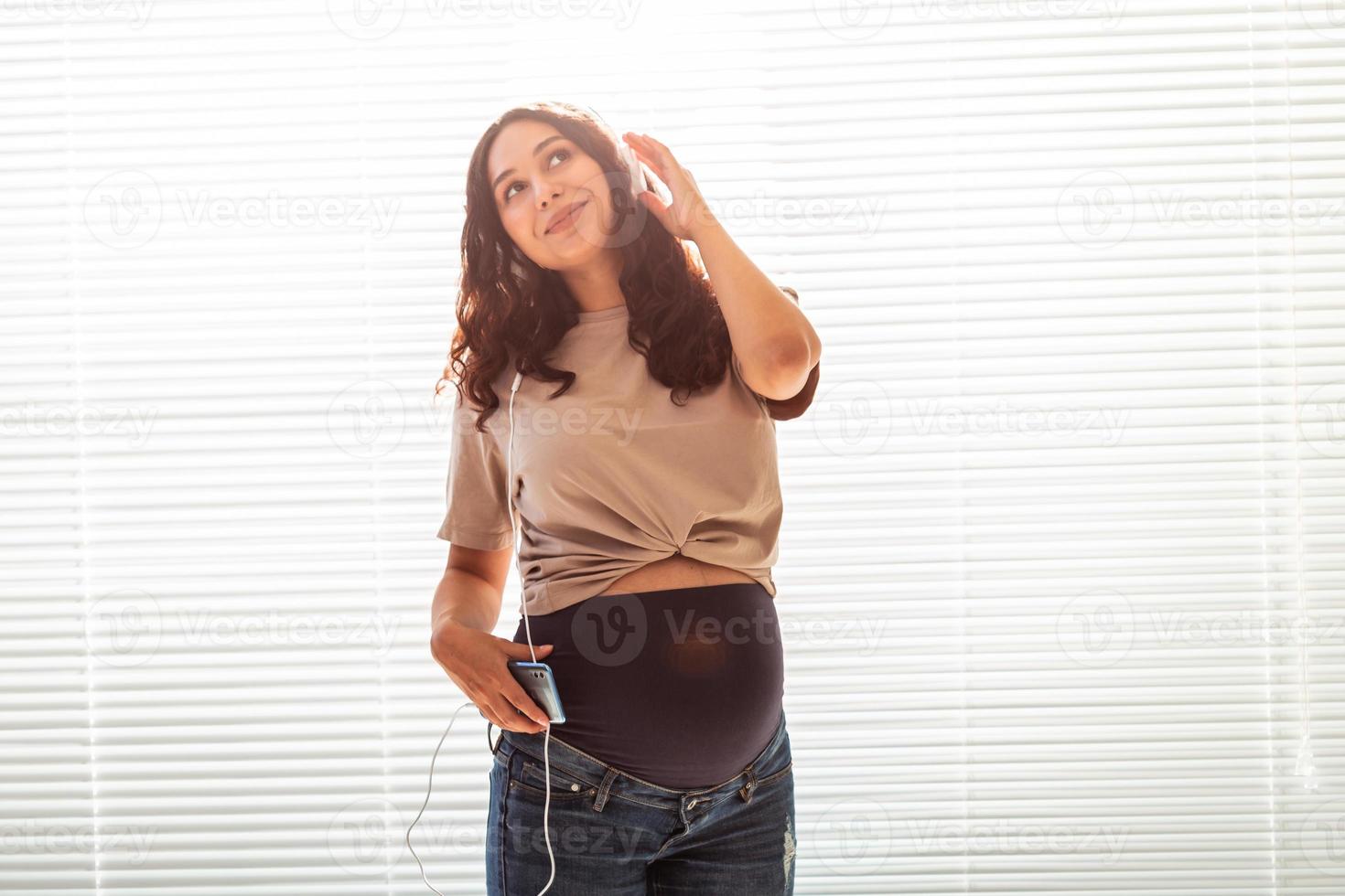 Beautiful young peaceful pregnant woman listens to pleasant classical music using smartphone and headphones. Concept of positive attitude before childbirth photo