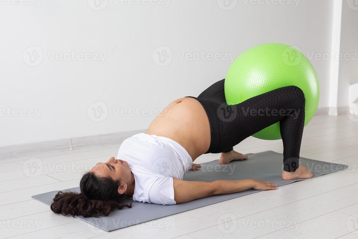 Young flexible pregnant woman doing gymnastics on rug on the floor on white background. The concept of preparing the body for easy childbirth photo