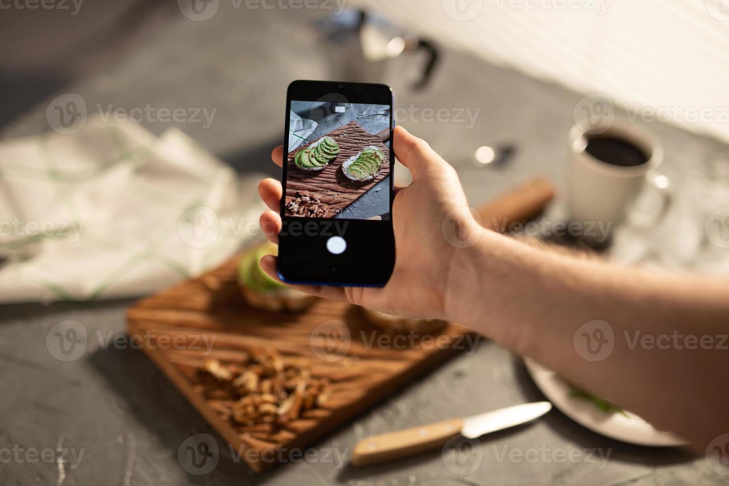 Hands take pictures on smartphone of two beautiful healthy sour cream and avocado sandwiches lying on board on the table. Social media and food concept photo