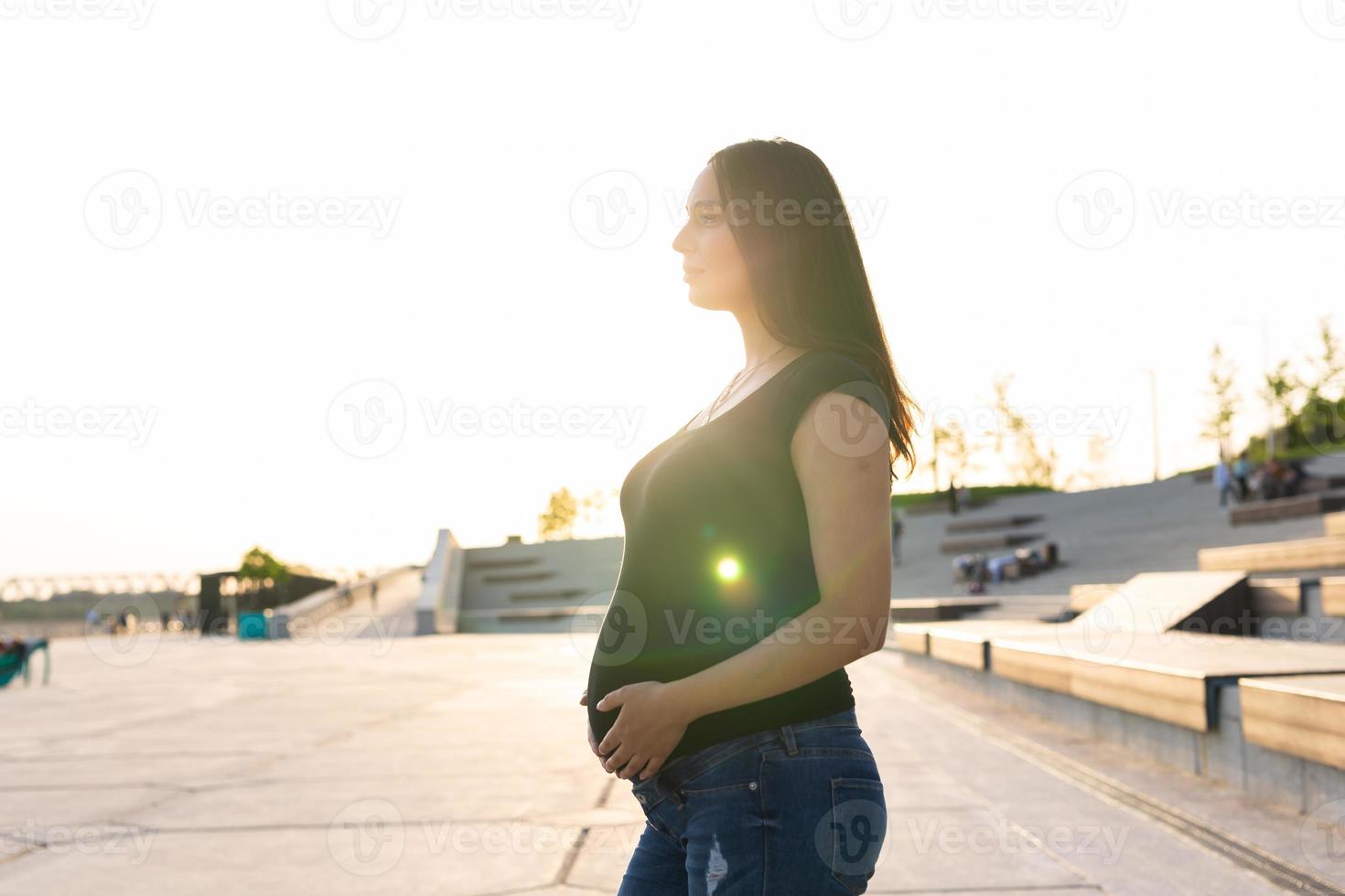 Pregnant hispanic woman on embankment, touching belly photo