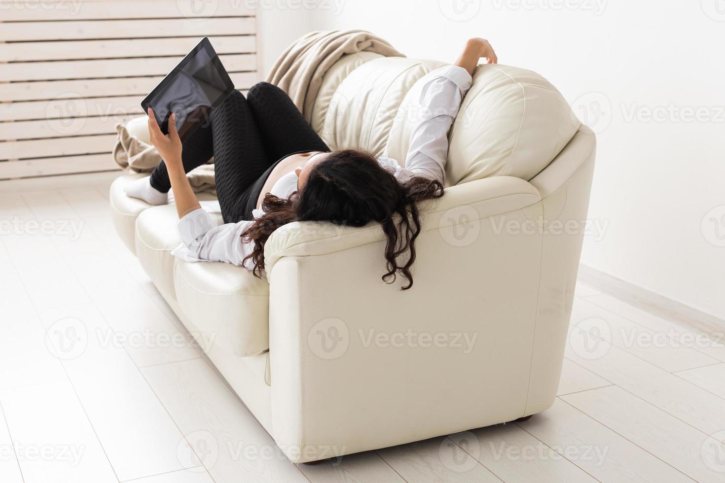 Latin pregnant woman using tablet computer while lying on sofa at home. Pregnancy and information for parenthood concept. photo