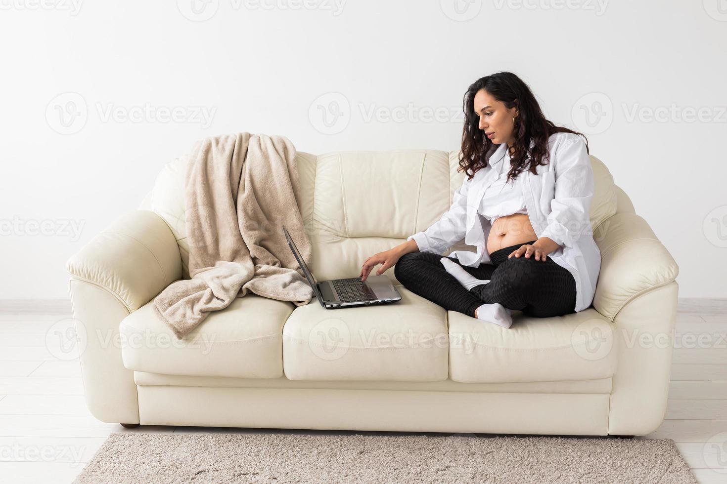 Pregnant woman using laptop while sitting on a couch in the living room