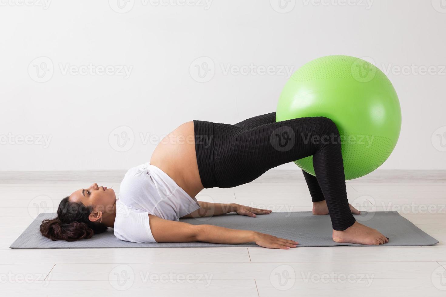 Young flexible pregnant woman doing gymnastics on rug on the floor on white background. The concept of preparing the body for easy childbirth photo