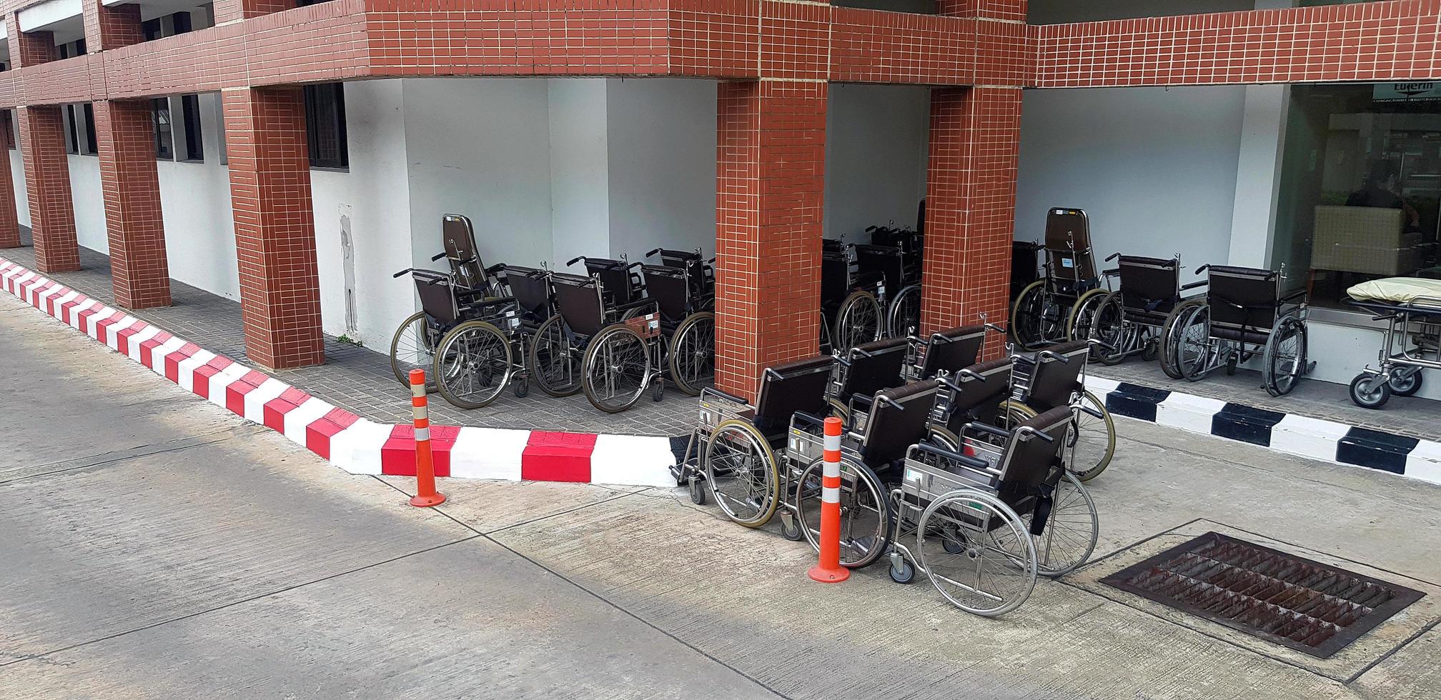 muchas sillas de ruedas o vehículos de transporte de pacientes estacionados en la acera cerca del edificio y la calle o la carretera en el hospital. equipo para ayudar a las personas que tienen dolor o lesiones. foto