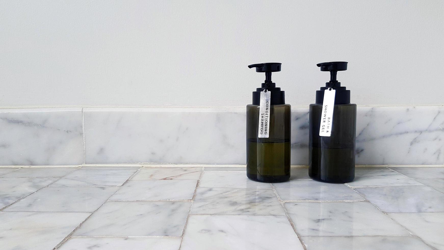 Two black plastic conditioner shampoo and bath shower gel putting on marble floor with white cement wall background with copy space on right. Cleaning part of body and Spa concept photo