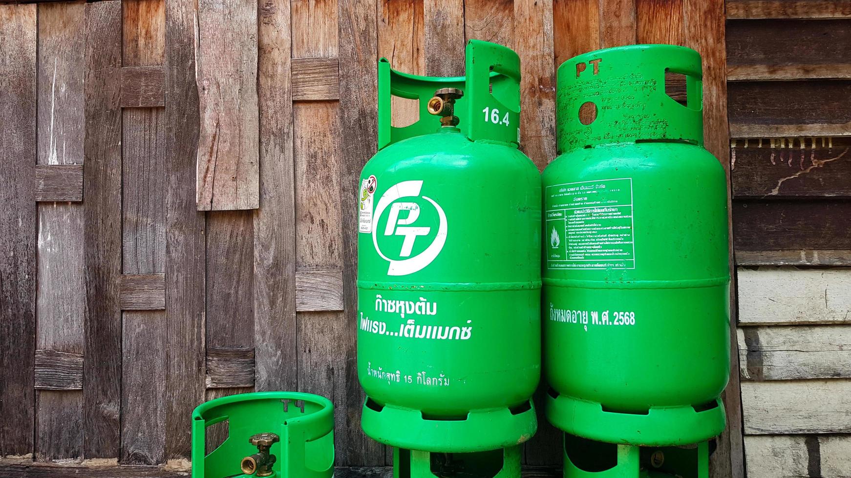 Bangkok, Thailand - January 2, 2022 Green gas tanks on wooden wall or wallpaper with copy space on left. Group of object to make fire for cooking food in kitchen. Energy or Dangerous equipment. photo