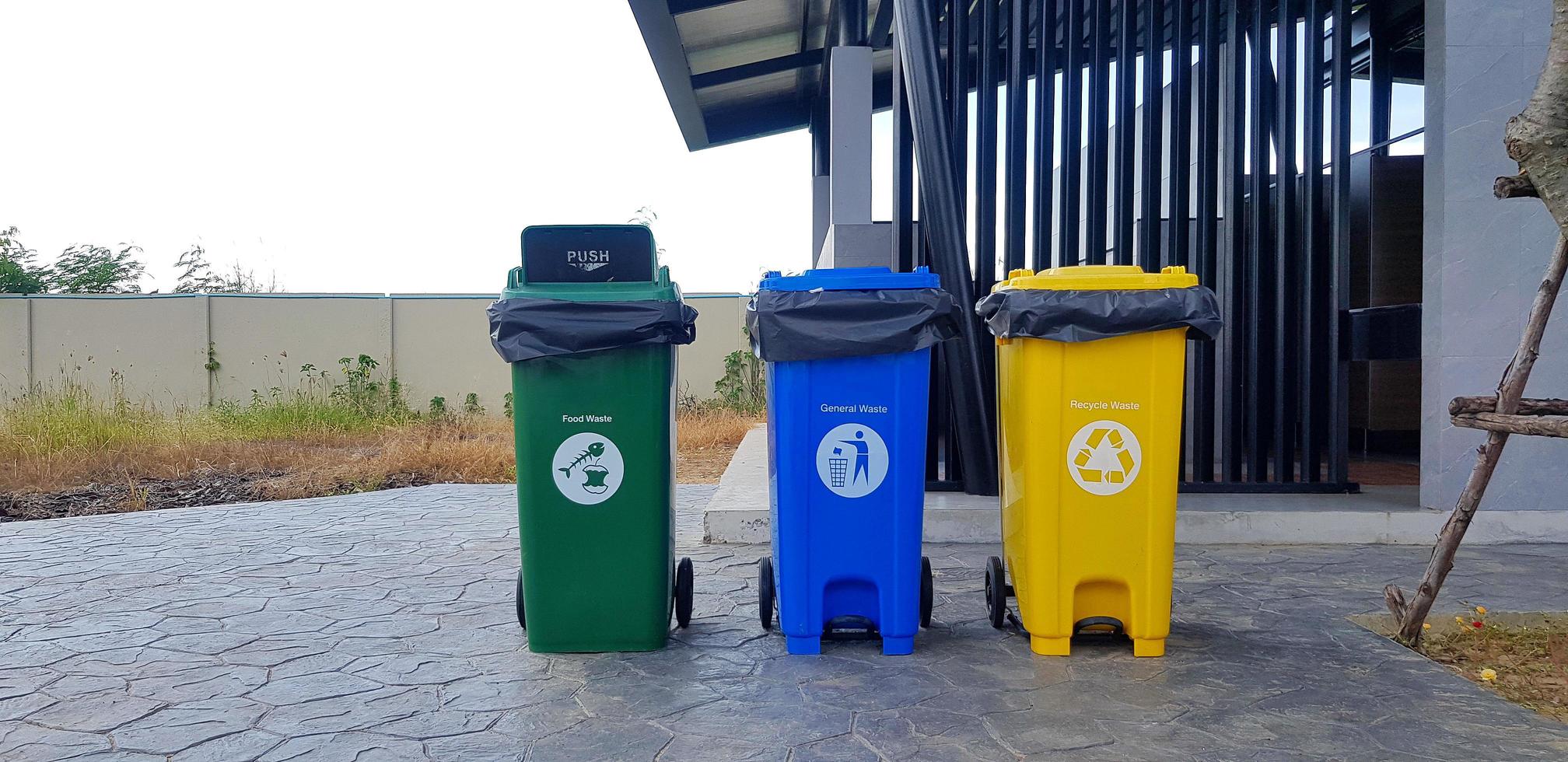 coloridos tres cubos de basura verde, azul, amarillo para separar la basura para su reutilización y eliminación frente al baño público o al baño. bote de basura para tirar cosas o material usado en la calle, camino o sendero. foto