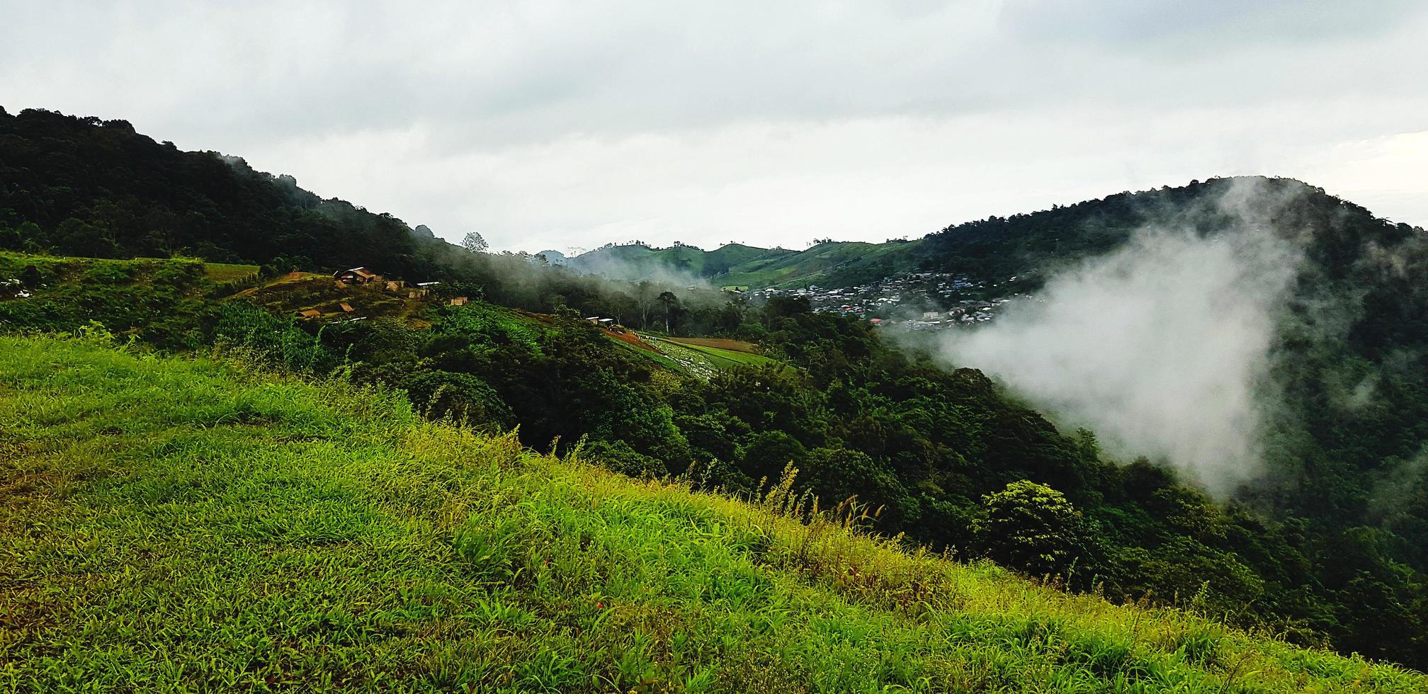 Beautiful range of green mountain, white cloud, small village and mist in the morning with copy space. Landscape view of hill at Phetchabun, Thailand. Natural wallpaper and Famous place for travel. photo