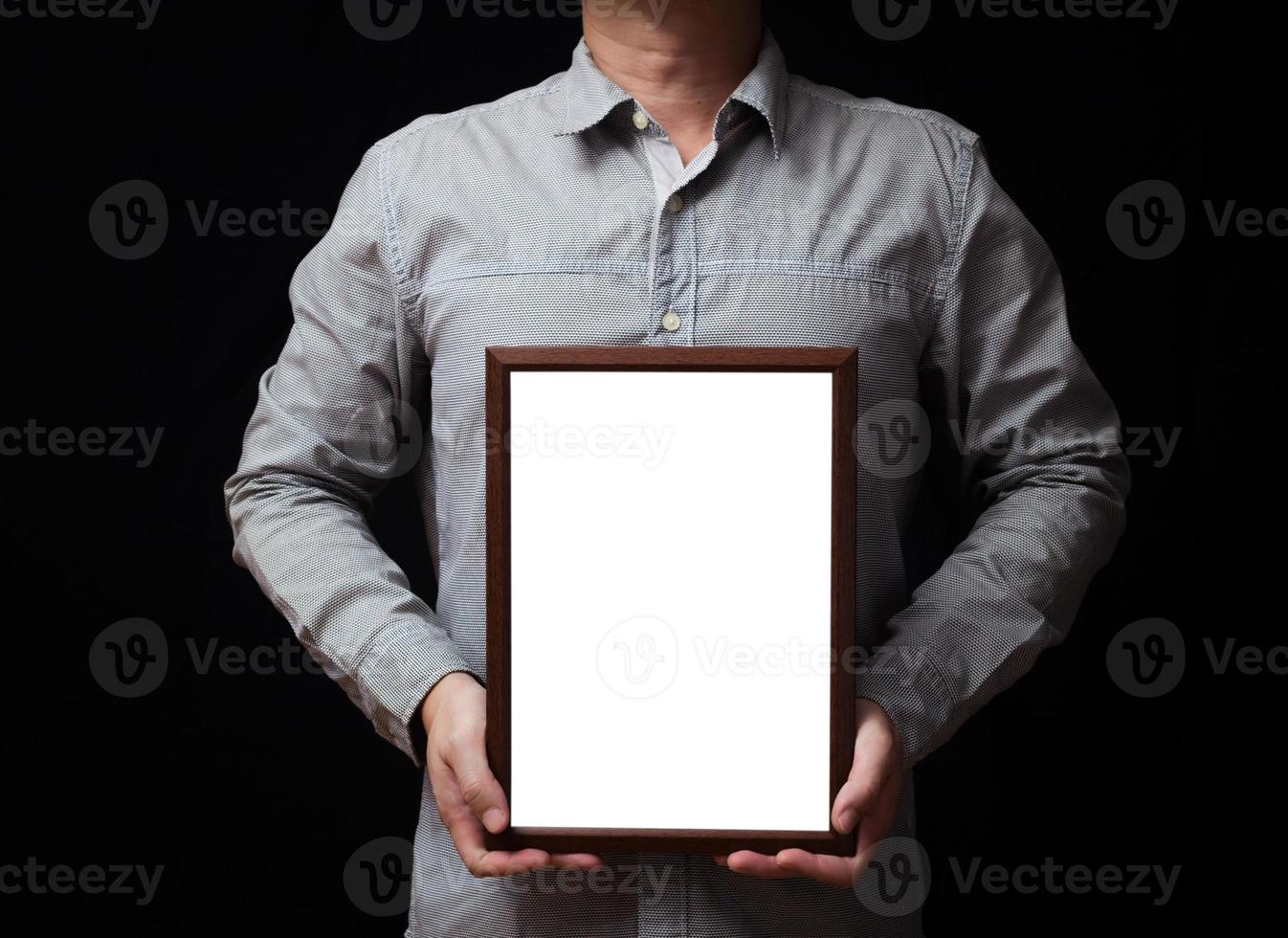 A blank diploma or a mockup certificate in the hand of a man employee wearing shirt on black background. The vertical picture frame is empty and the copy space. photo