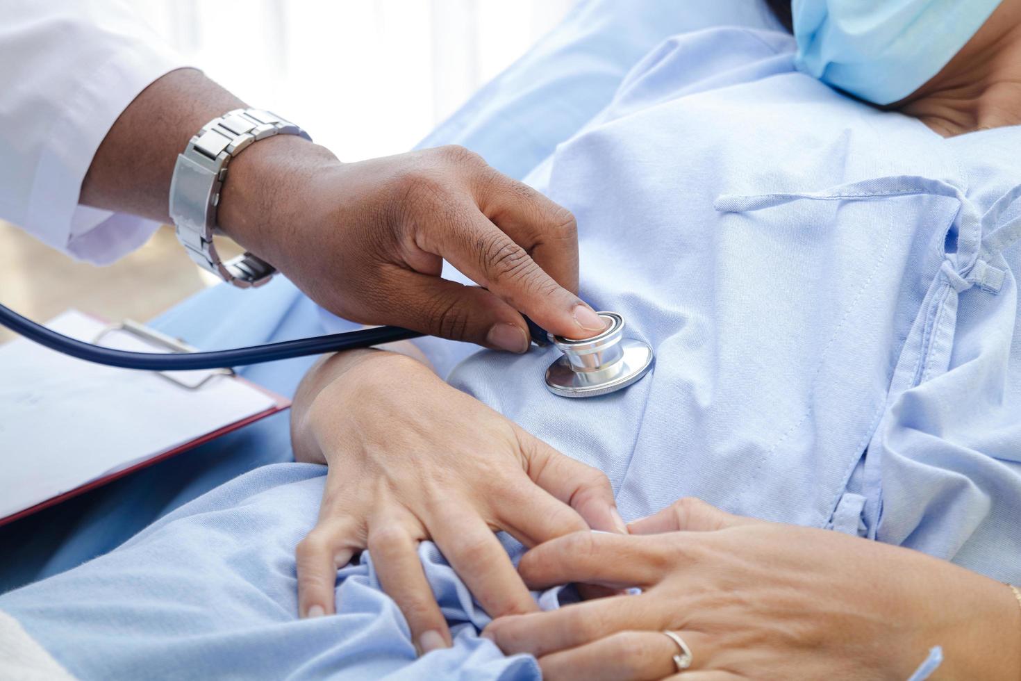 African American male doctor Check the illness of a woman lying in a hospital bed. Treatment of patients during the coronavirus epidemic. Concept of medical service. photo