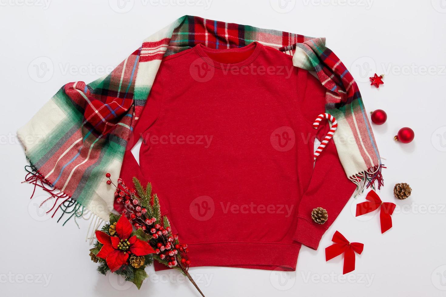 Close up red blank template sweatshirt with copy space and Christmas Holiday concept. Top view mockup hoodie and red holidays decorations on white background. Happy New Year accessories. Xmas outfit photo