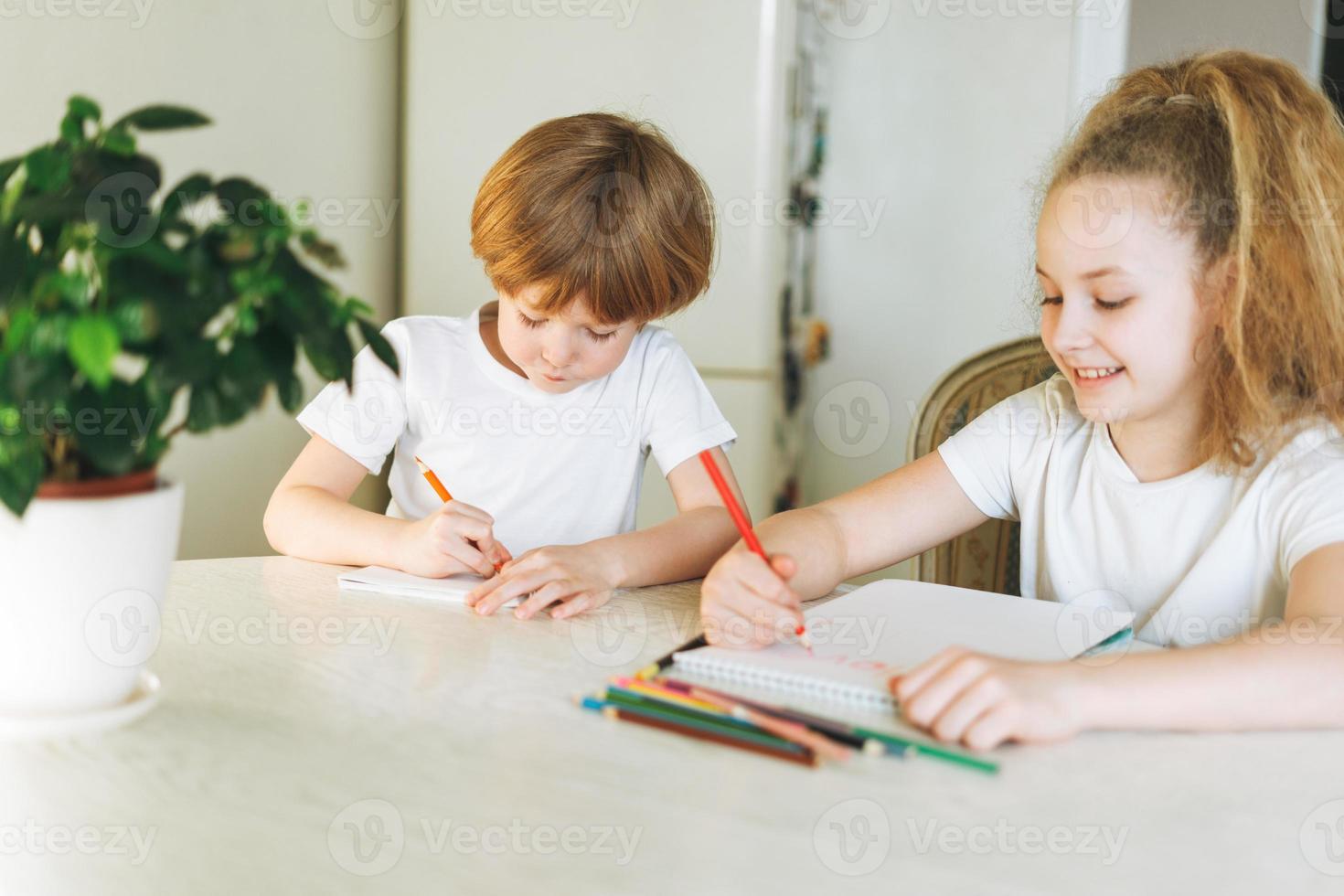 Two siblings brother and sister toddler boy tween girl drawing on table in kitchen at home photo