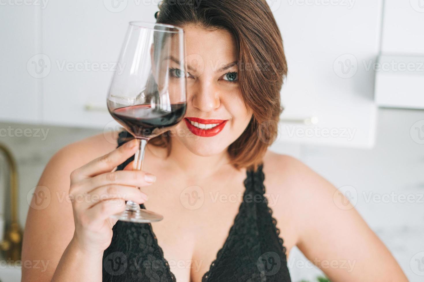 Beautiful happy sensual brunette young woman plus size body positive with glass of red wine enjoying her life at home photo