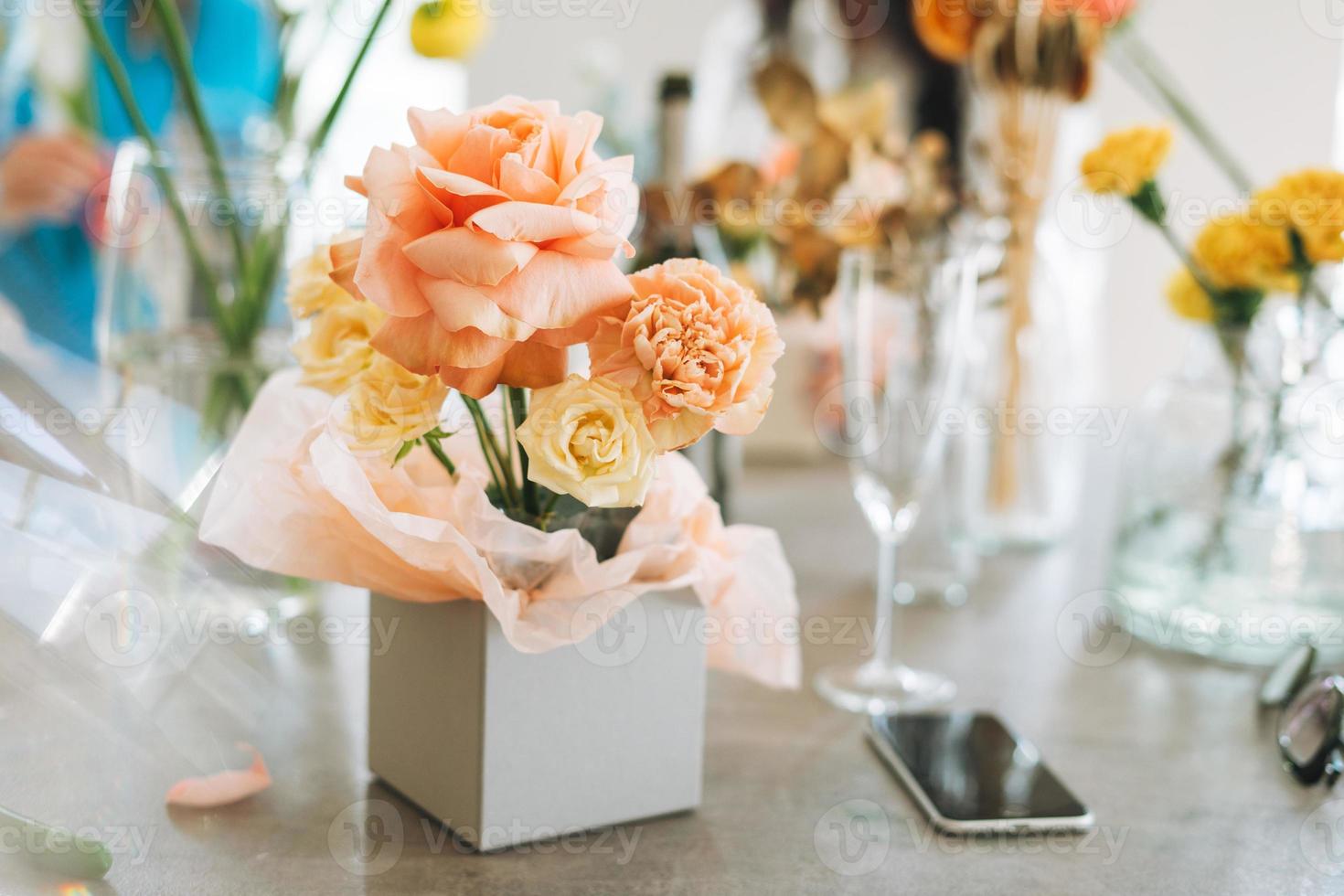 Flower arrangement with yellow and pink roses in gift box on table in flower shop, modern floristic working place photo