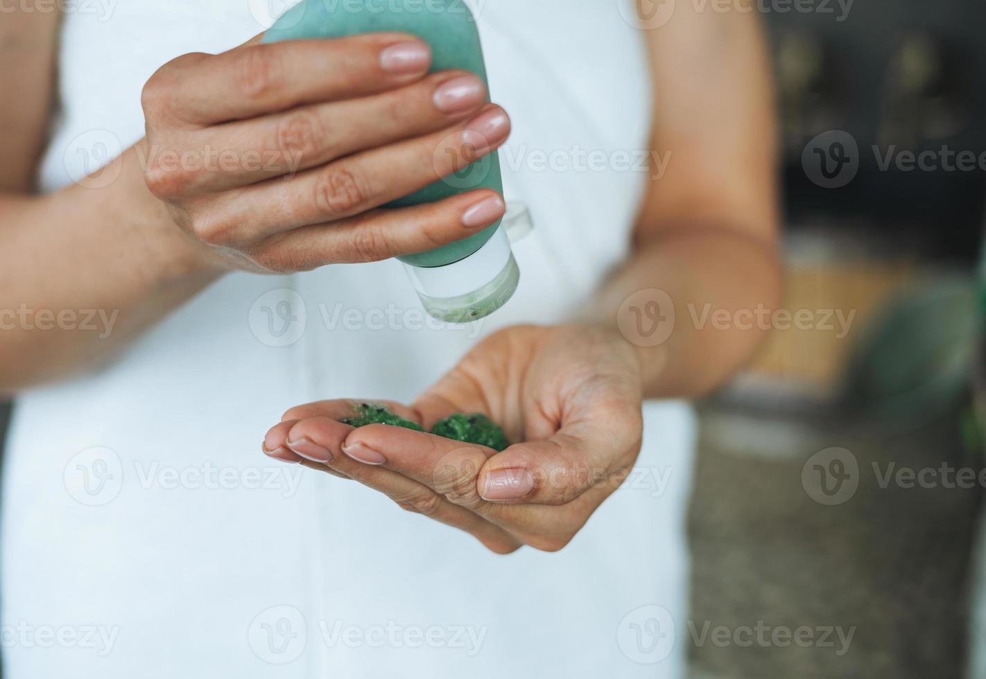 mujer joven con toalla blanca sostiene un frasco de matorral natural en el baño, rutina matutina de cuidado corporal foto