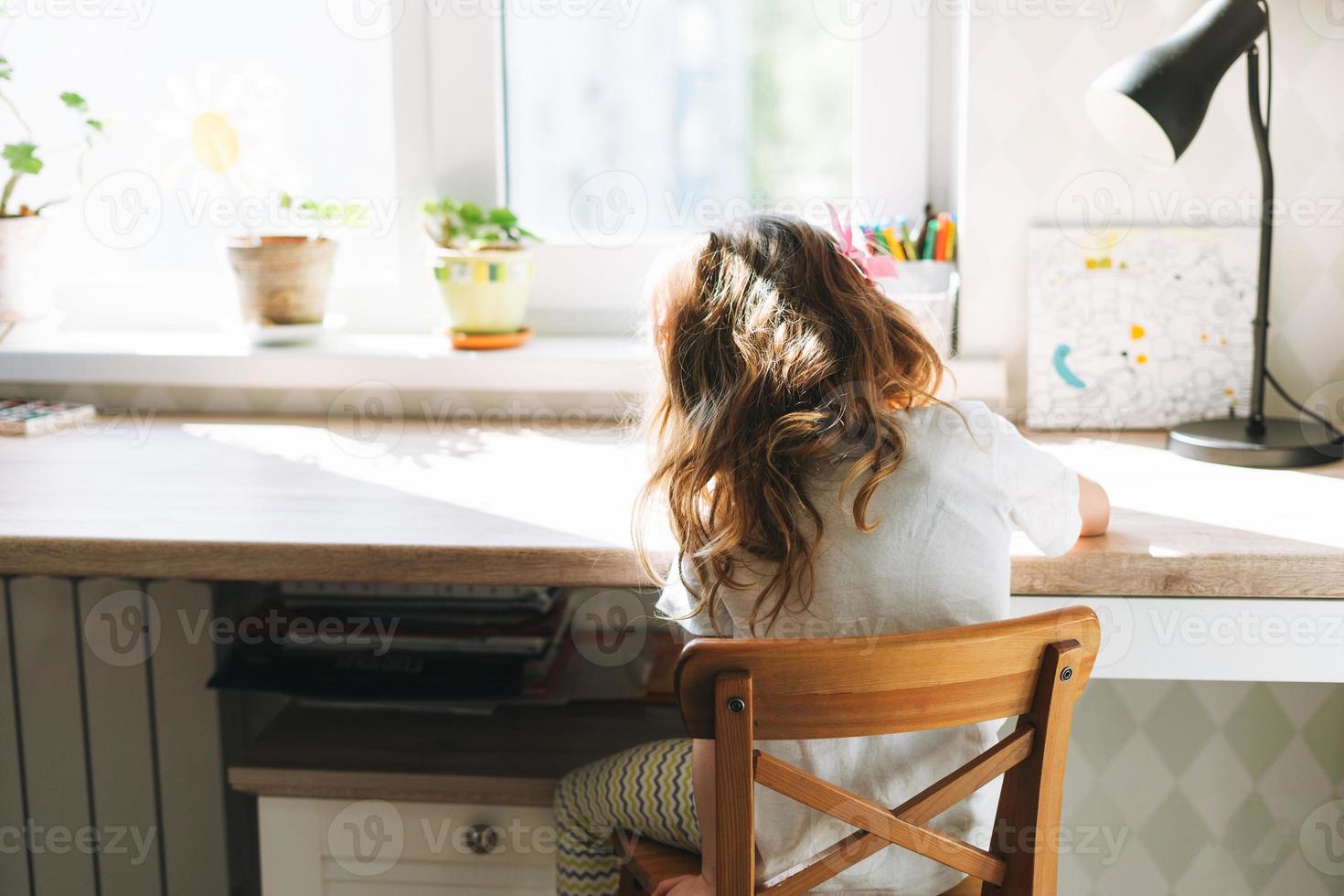 Little child beautiful girl with long hair in home clothes painting at desk in children room at the home photo