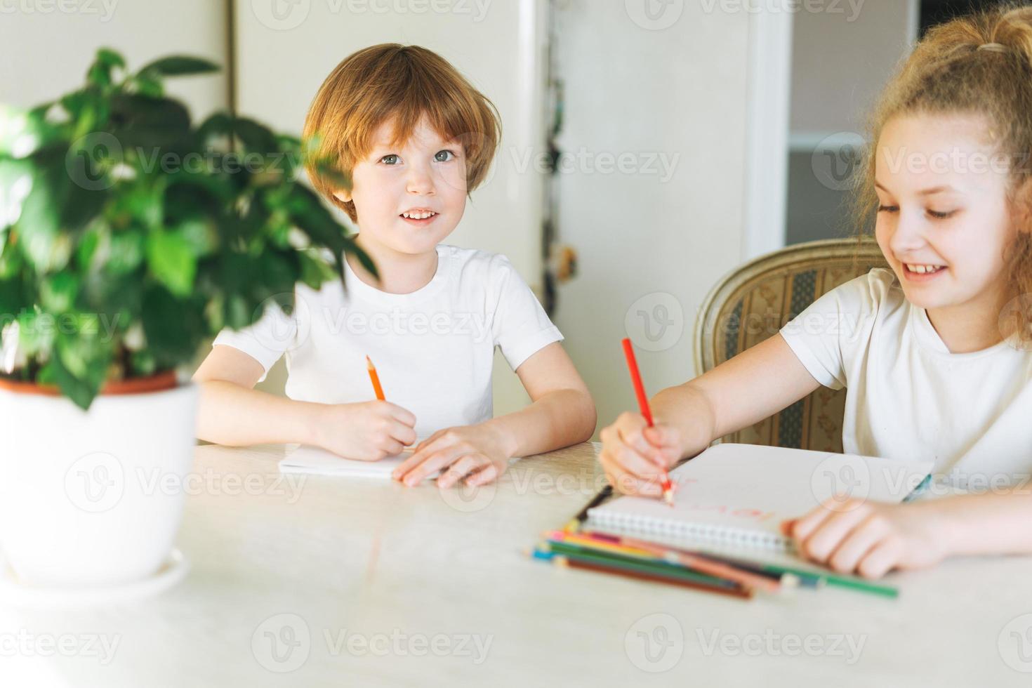 Two siblings brother and sister toddler boy tween girl drawing on table in kitchen at the home photo