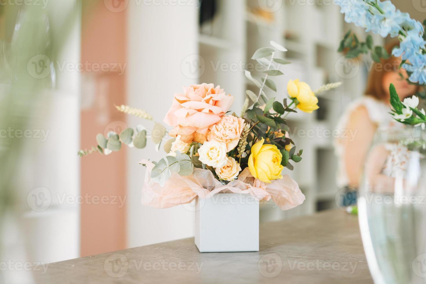 Flower arrangement with yellow and pink roses and eucalyptus in gift box on table in the flower shop, modern floristic photo