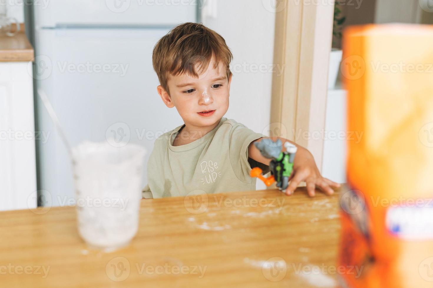 el niño pequeño se divierte mientras cocina con harina en la mesa de la cocina en casa. niño jugando con el juguete foto