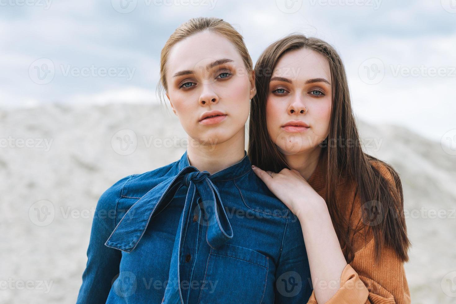 Fashion beauty portrait of young women sisters in brown organic velvet jeans shirts on the desert background photo