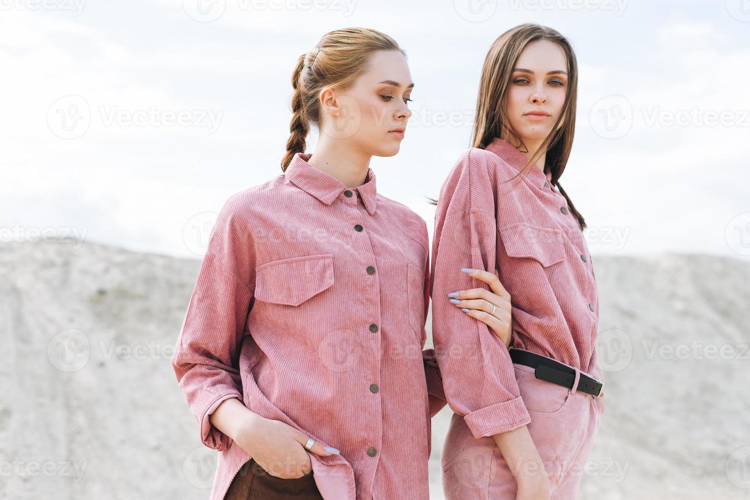 Fashion beauty portrait of young women sisters in pink organic velvet shirts on desert background photo
