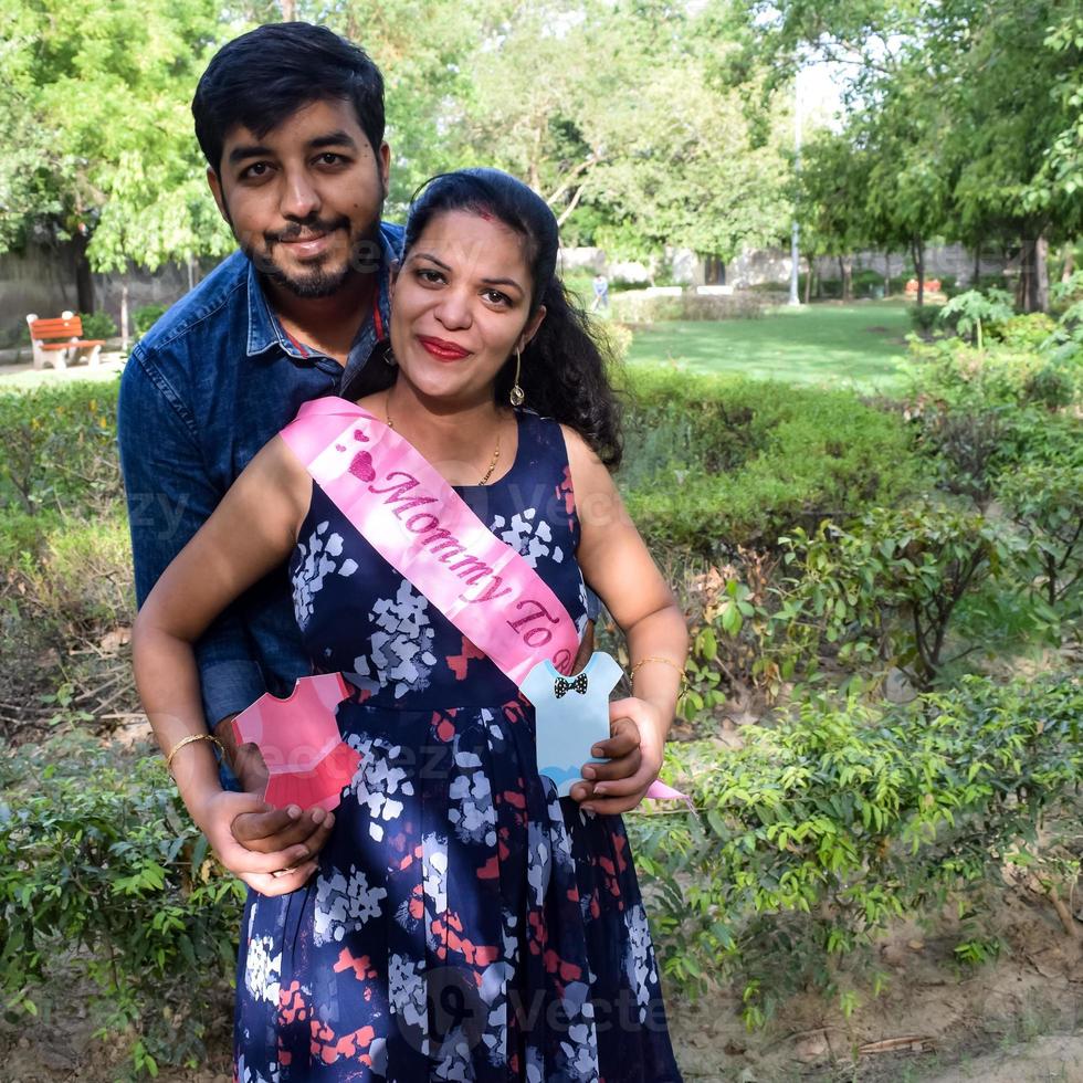 Indian couple posing for maternity baby shoot. The couple is posing in a lawn with green grass and the woman is falunting her baby bump in Lodhi Garden in New Delhi, India photo