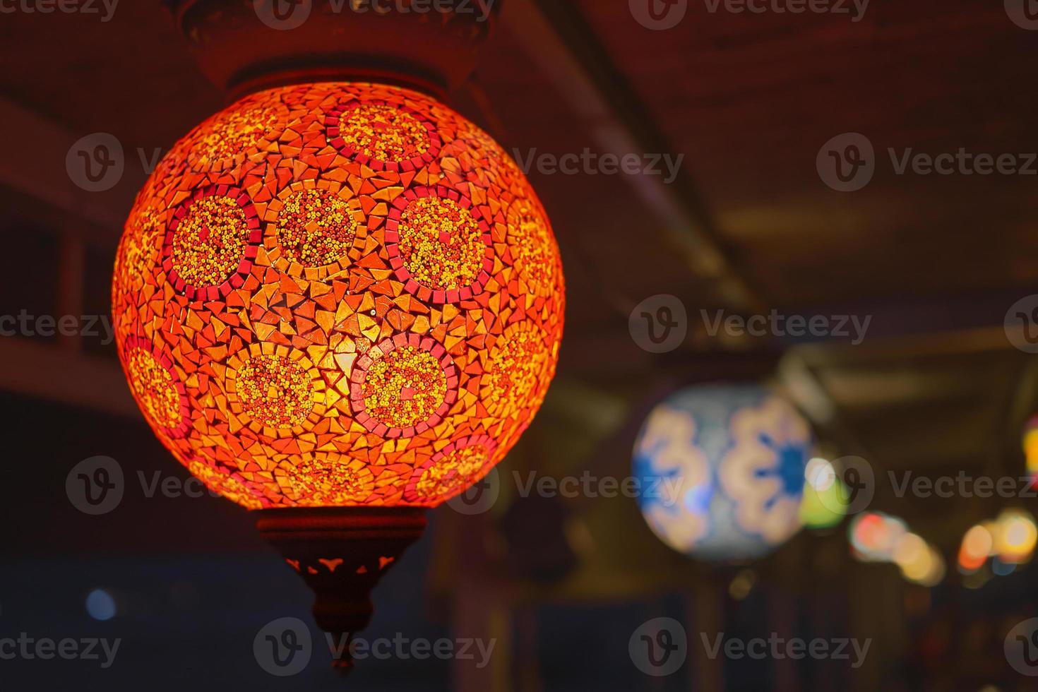 Glowing red traditional colorful Turkish lamp or handmade lantern, selective focus on lantern, blurred background, popular souvenir lanterns in cafe photo