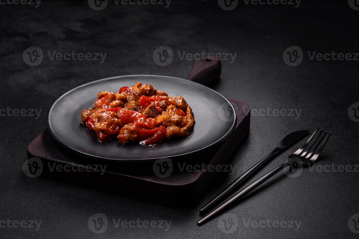 Delicious juicy meat with hot peppers and sauce on a black ceramic plate photo