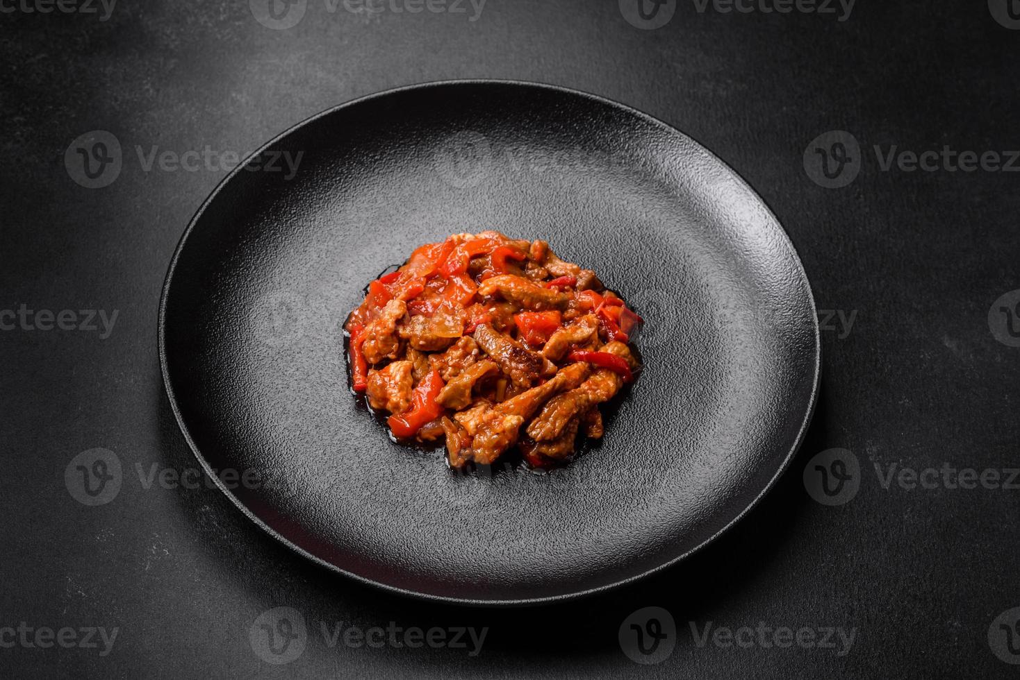 Delicious juicy meat with hot peppers and sauce on a black ceramic plate photo