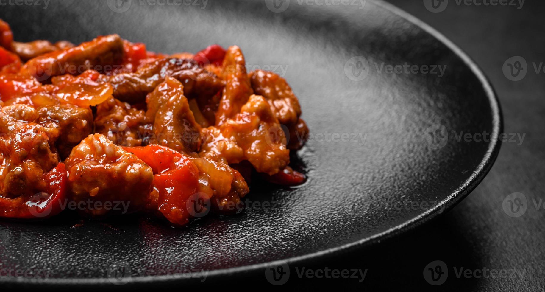 Delicious juicy meat with hot peppers and sauce on a black ceramic plate photo