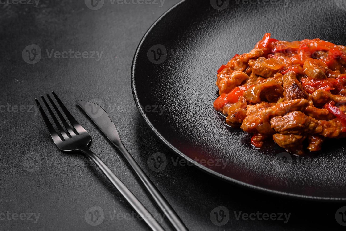 Delicious juicy meat with hot peppers and sauce on a black ceramic plate photo