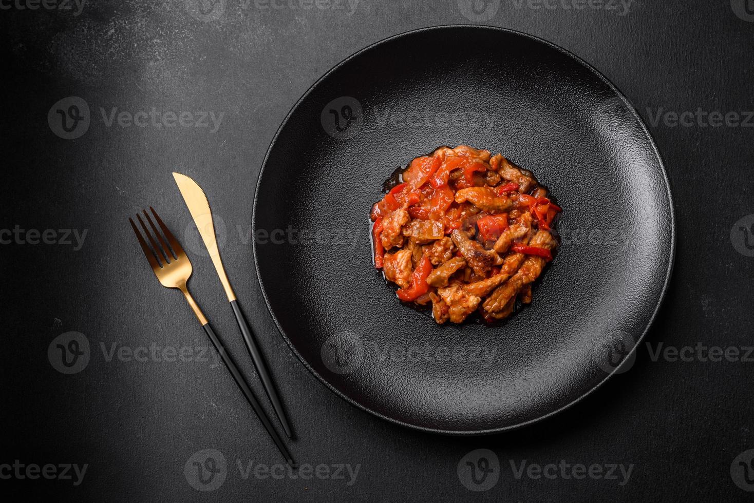 Delicious juicy meat with hot peppers and sauce on a black ceramic plate photo