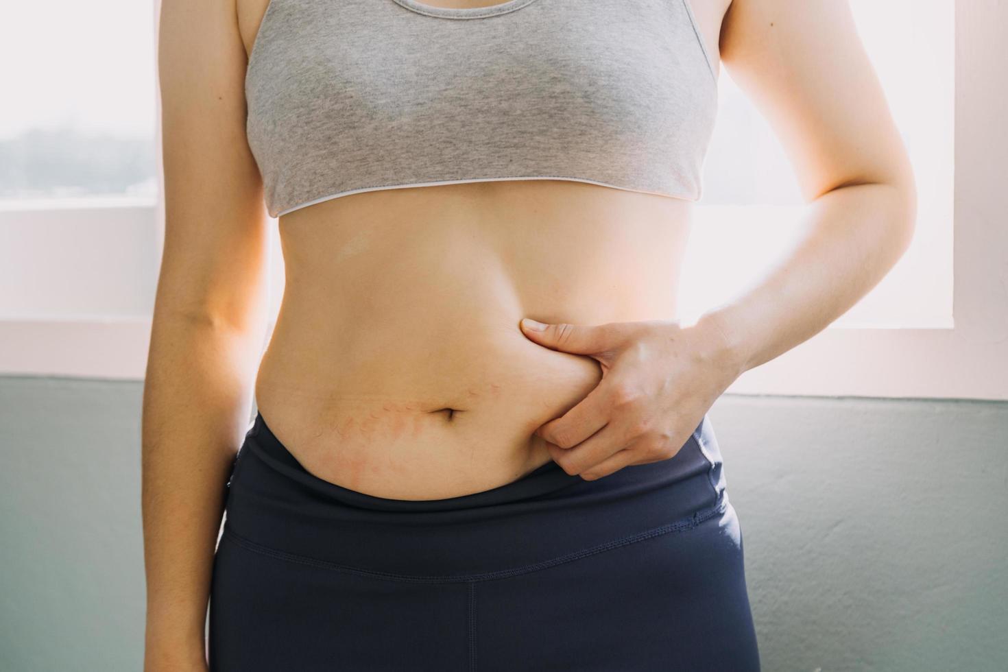 hermosa mujer gorda con cinta métrica usa su mano para exprimir el exceso de grasa que está aislado en un fondo blanco. ella quiere perder peso, el concepto de cirugía y descomponer grasa bajo el foto