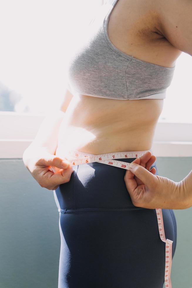 hermosa mujer gorda con cinta métrica usa su mano para exprimir el exceso de grasa que está aislado en un fondo blanco. ella quiere perder peso, el concepto de cirugía y descomponer grasa bajo el foto