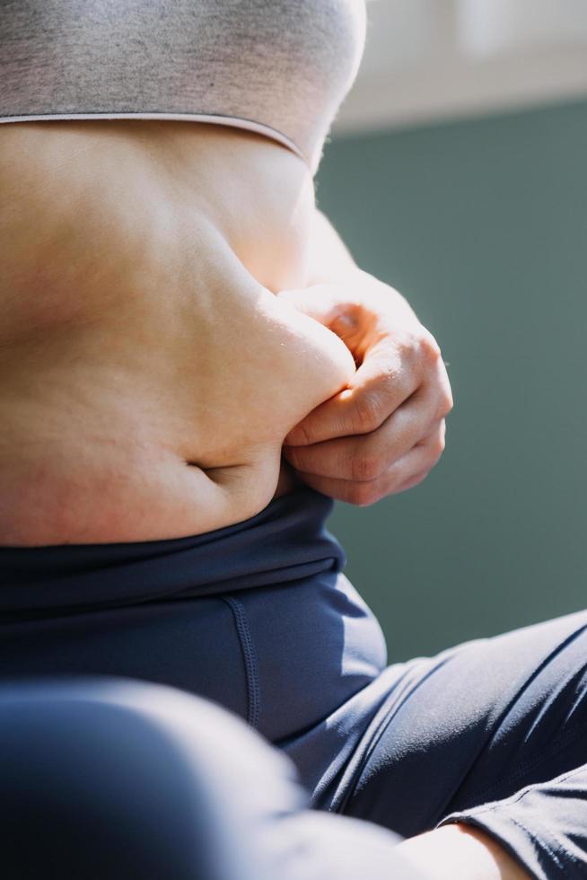 hermosa mujer gorda con cinta métrica usa su mano para exprimir el exceso de grasa que está aislado en un fondo blanco. ella quiere perder peso, el concepto de cirugía y descomponer grasa bajo el foto