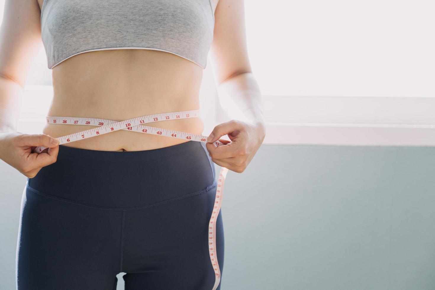 hermosa mujer gorda con cinta métrica usa su mano para exprimir el exceso de grasa que está aislado en un fondo blanco. ella quiere perder peso, el concepto de cirugía y descomponer grasa bajo el foto