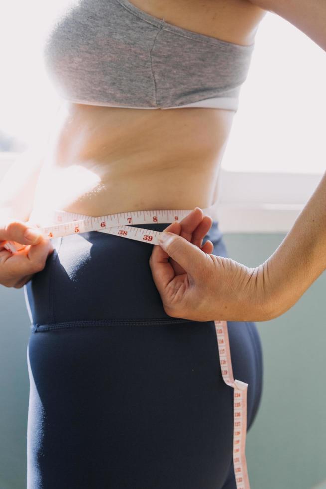 hermosa mujer gorda con cinta métrica usa su mano para exprimir el exceso de grasa que está aislado en un fondo blanco. ella quiere perder peso, el concepto de cirugía y descomponer grasa bajo el foto