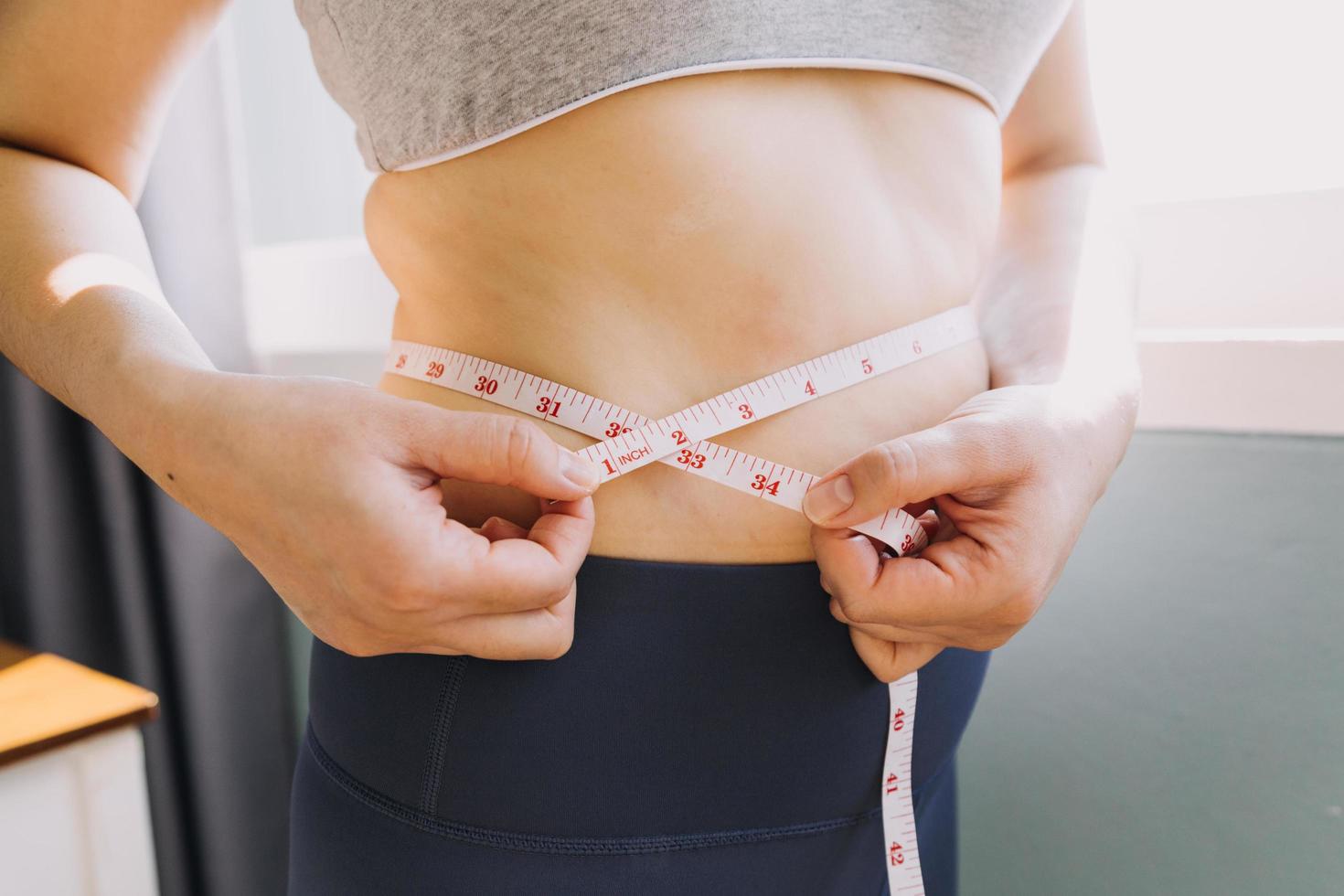 hermosa mujer gorda con cinta métrica usa su mano para exprimir el exceso de grasa que está aislado en un fondo blanco. ella quiere perder peso, el concepto de cirugía y descomponer grasa bajo el foto