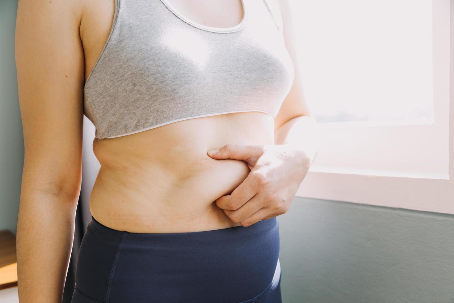 hermosa mujer gorda con cinta métrica usa su mano para exprimir el exceso de grasa que está aislado en un fondo blanco. ella quiere perder peso, el concepto de cirugía y descomponer grasa bajo el foto