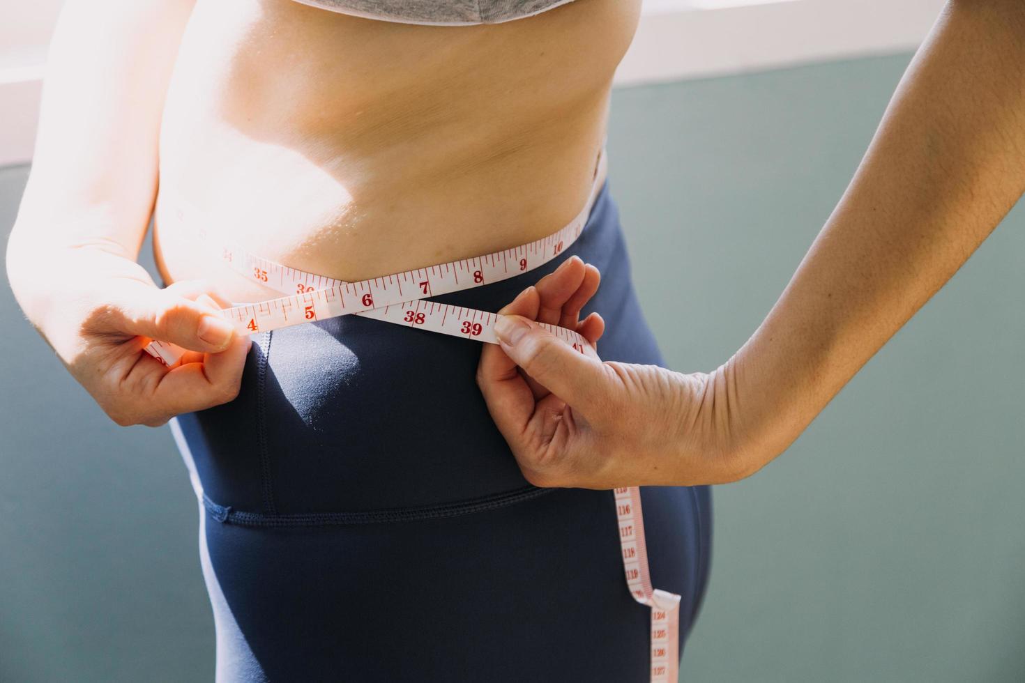 hermosa mujer gorda con cinta métrica usa su mano para exprimir el exceso de grasa que está aislado en un fondo blanco. ella quiere perder peso, el concepto de cirugía y descomponer grasa bajo el foto