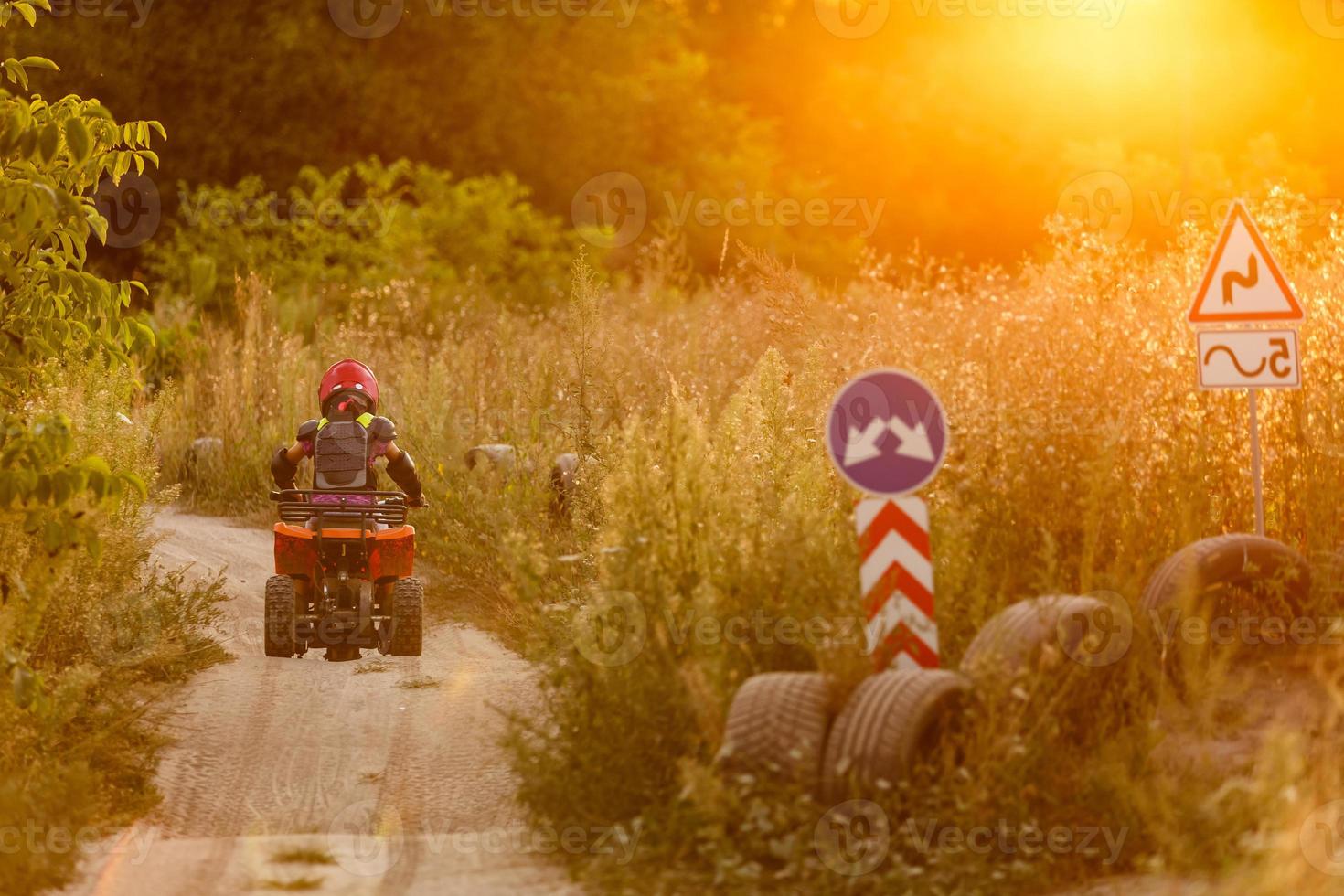 Happy little girl playing on road at the day time. He driving on quad bike in the park. Child having fun on the nature. Concept of happiness. photo