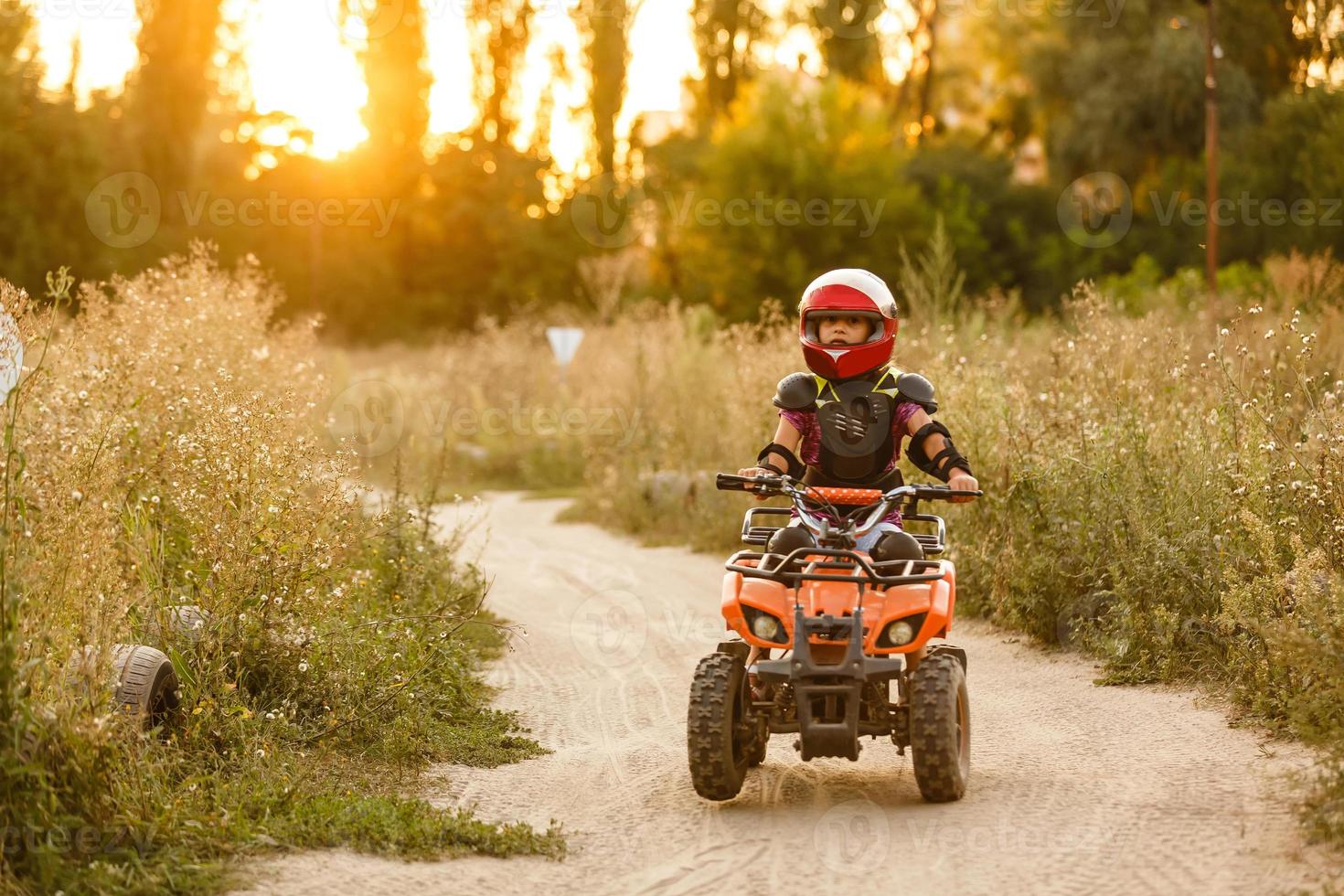 la niña monta un quad atv. una mini quad es una chica genial con casco y ropa protectora. El coche eléctrico de quad eléctrico para niños populariza la tecnología ecológica. foto