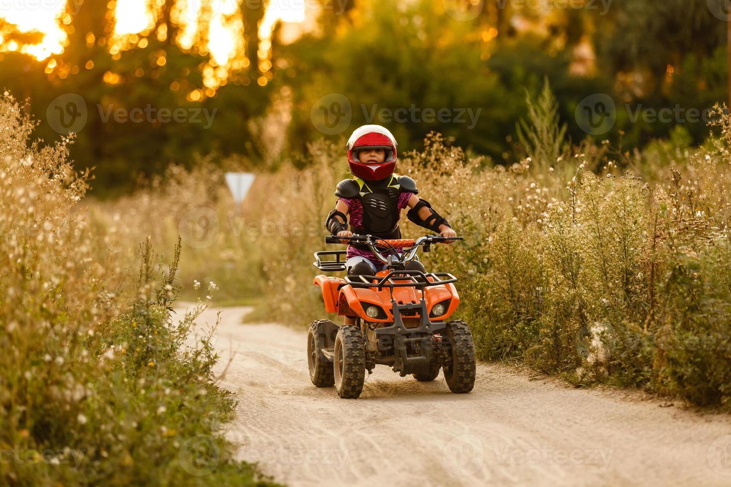 la niña monta un quad atv. una mini quad es una chica genial con casco y ropa protectora. El coche eléctrico de quad eléctrico para niños populariza la tecnología ecológica. foto