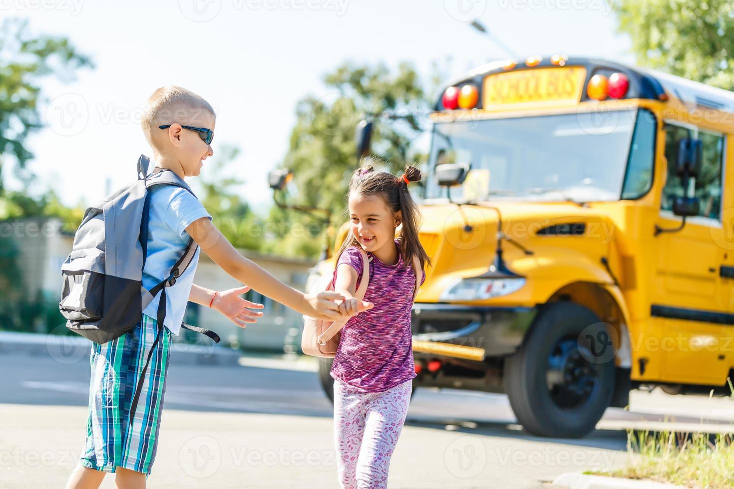 beautiful little schoolgirl with classmates near school bus photo