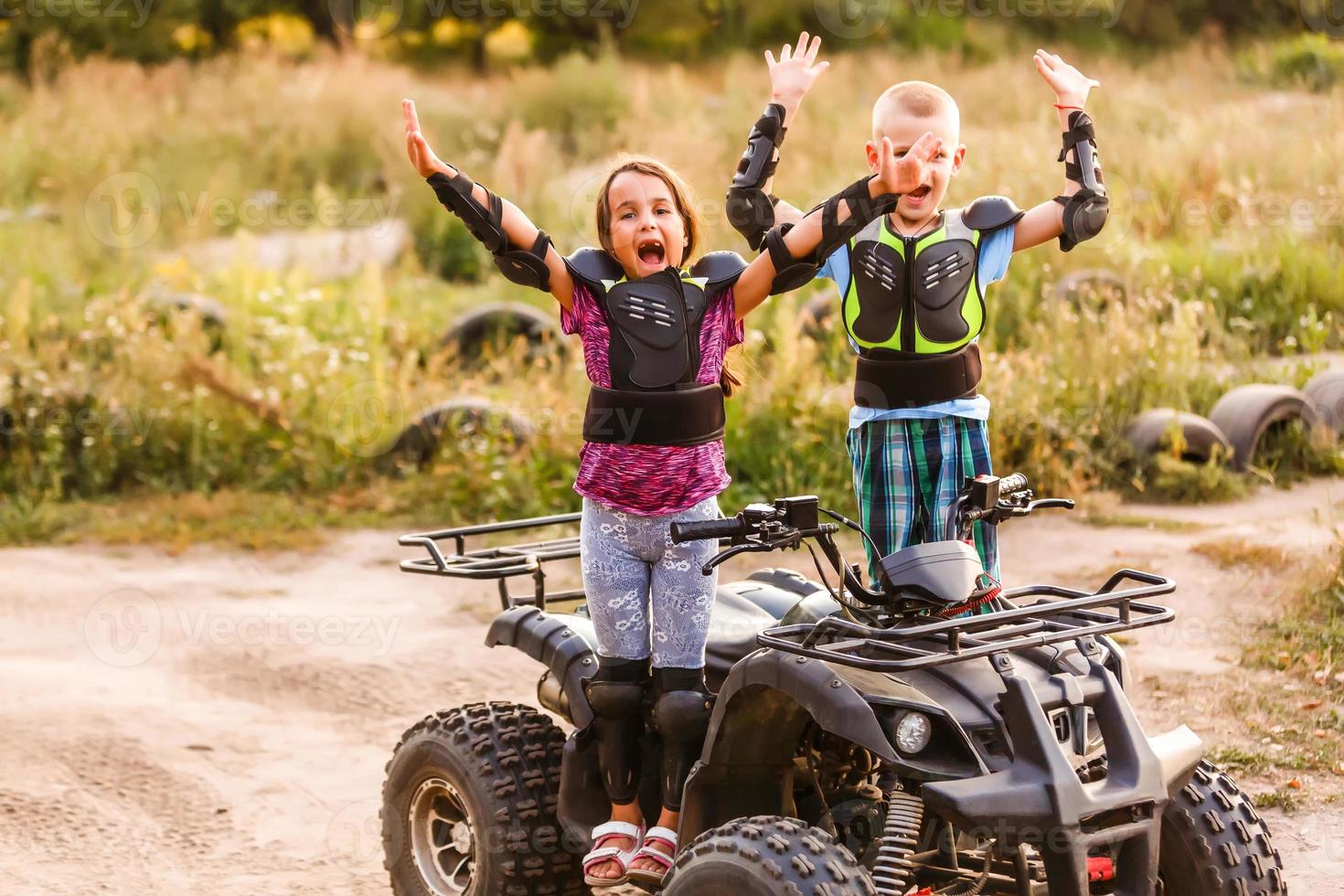 Happy little children playing on road at the day time. They driving on quad bike in the park. Kids having fun on the nature. Concept of happiness. photo